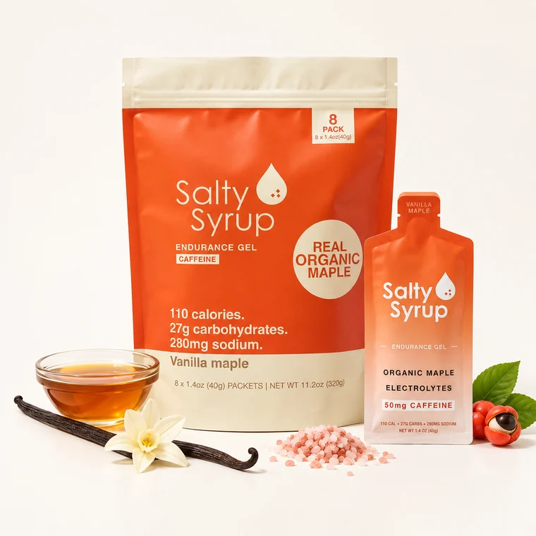 One orange and cream Salty Syrup Caffeinated bag with an 8 PACK badge and a single gel pouch, beside a small bowl of maple syrup, a vanilla pod and pink salt.