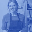 A person in an apron, smiling in an indoor setting, in monochrome blue.