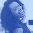 A cheerful woman with curly hair, smiling broadly and slightly turned, in monochrome blue.